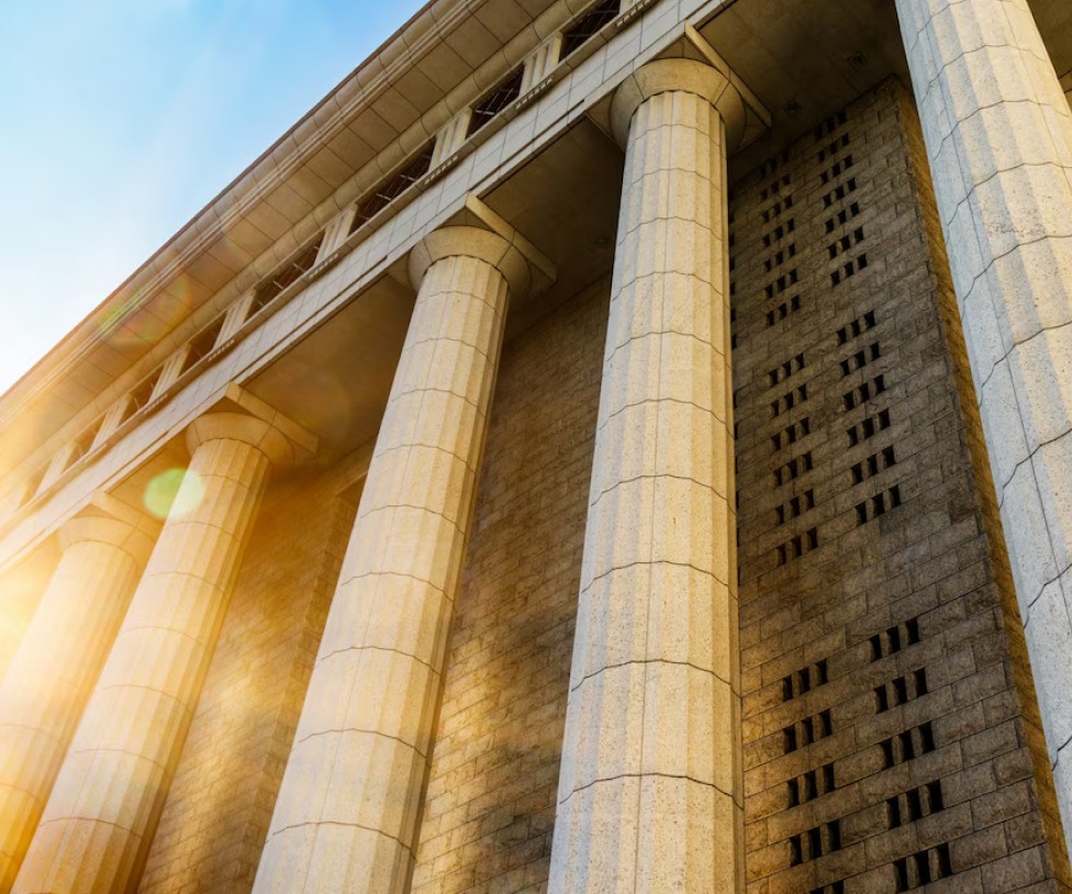 Grand courthouse building with tall stone columns and sunlight shining through.