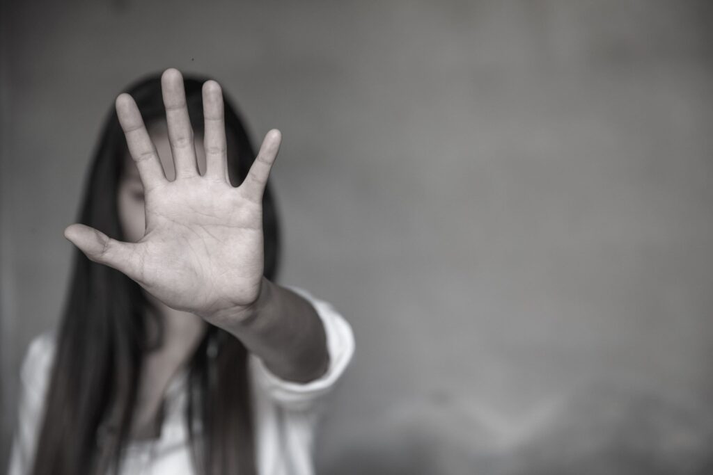 A woman extending her hand forward in a stop gesture, symbolizing resistance, protection, or a call to end violence and abuse.